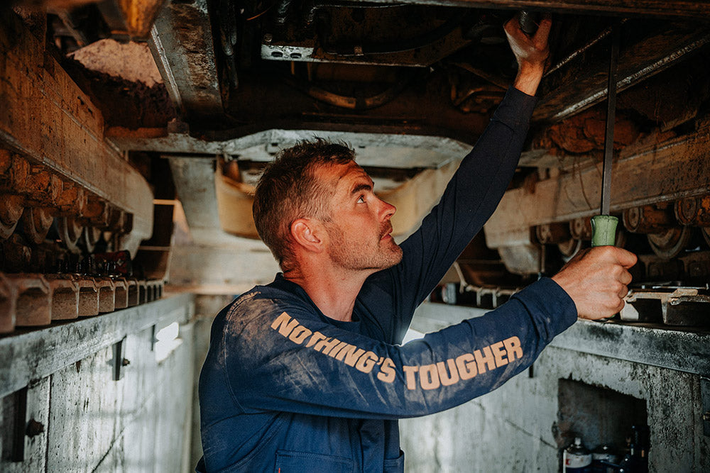 Person working underneath a vehicle with 'Nothing's Tougher' text on their sleeve.
