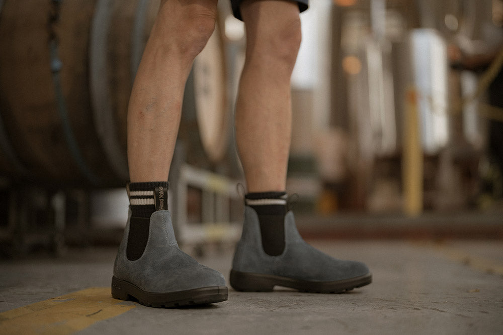 Person wearing gray Chelsea boots with black soles in a warehouse setting.
