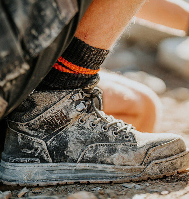 Dirtied work boot with orange and black sock on a blurred outdoor background