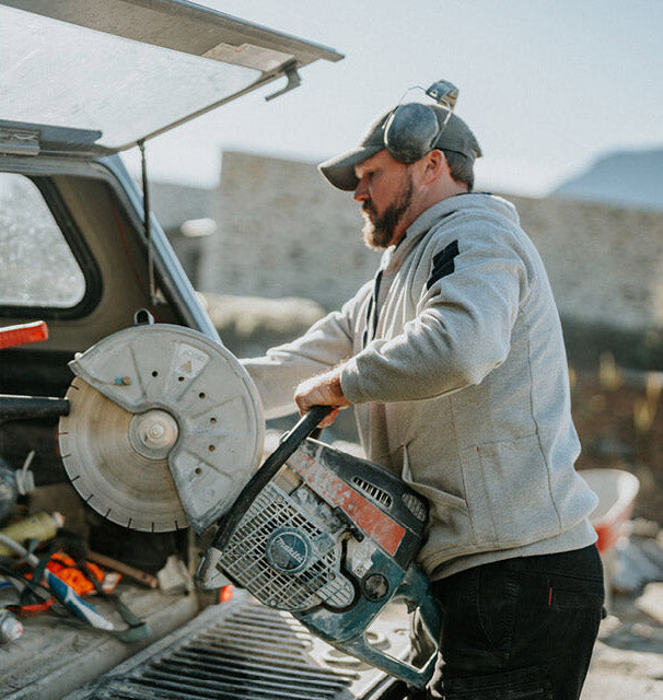 Man holding a chainsaw next to an open car trunk outdoors