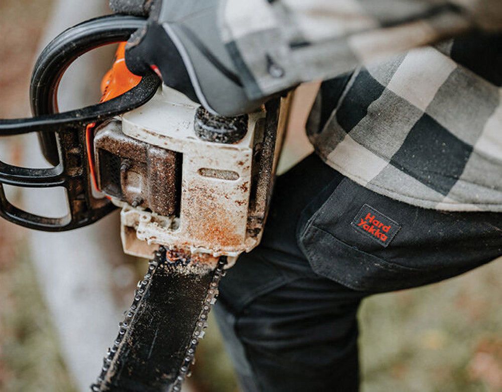 Person holding a chainsaw with a checkered shirt and dark pants.