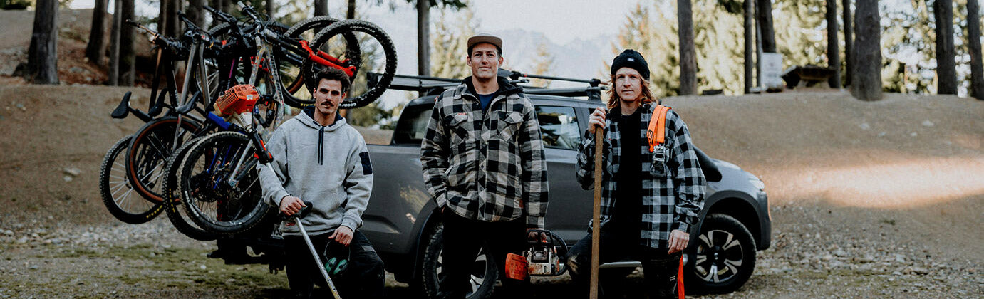 Two people standing next to a car with bicycles attached, in a forested area.