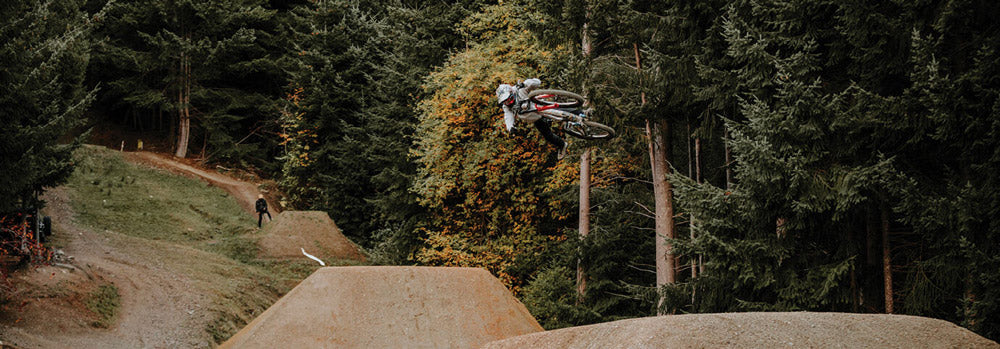Biker in mid-air over a dirt jump with trees in the background