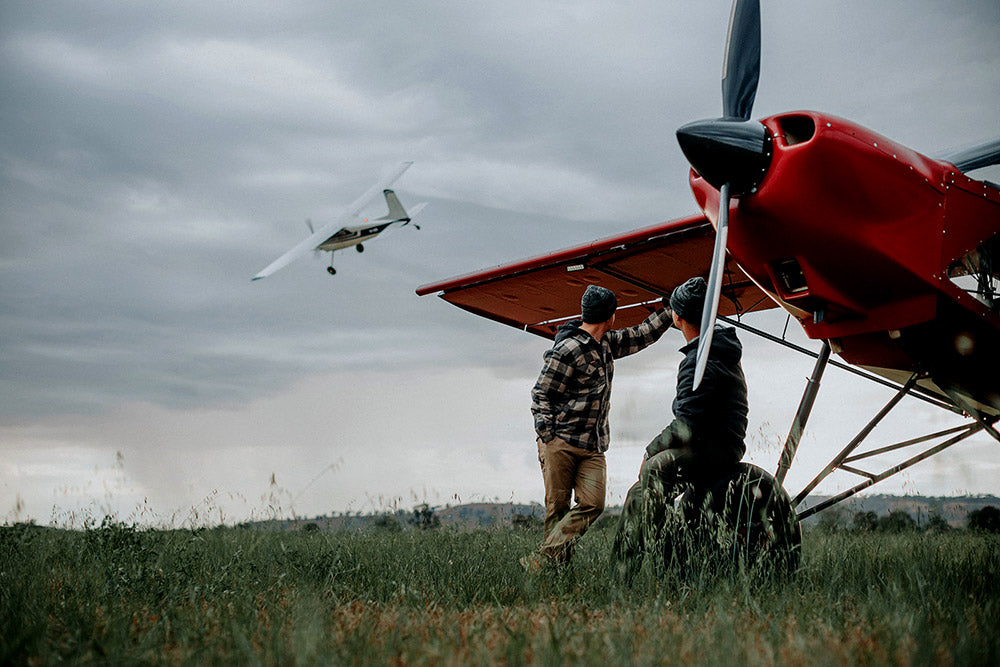 Two people with a red airplane in a grassy field on a cloudy day.