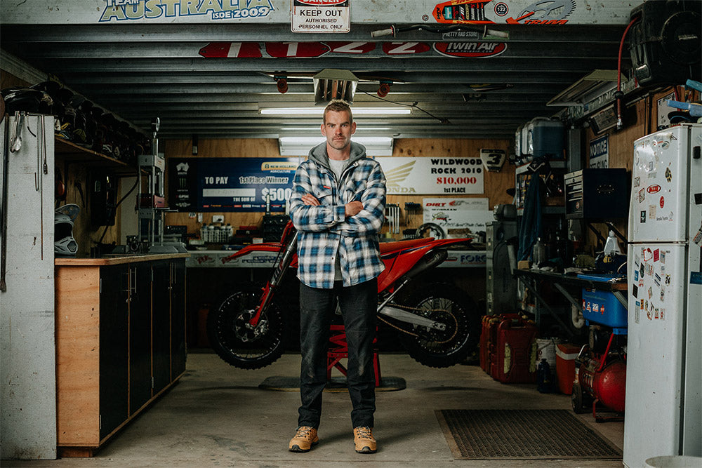 Man standing in a garage with a motorcycle and various items in the background