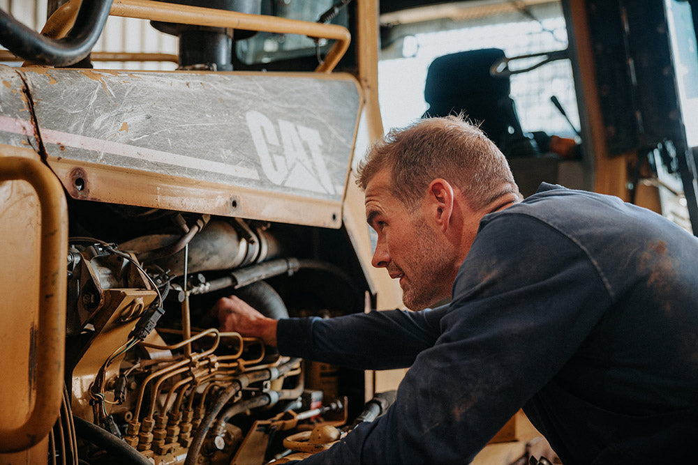Man working on the engine of a large piece of machinery, possibly a truck or bus.