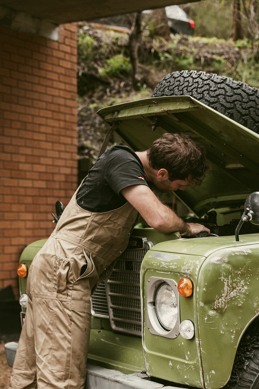 Person working on a vintage green vehicle with an open hood outdoors.