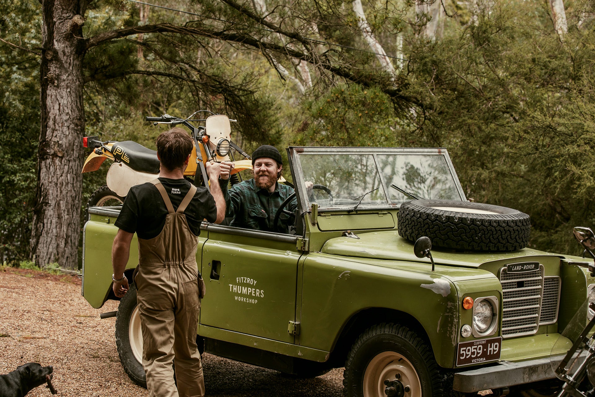 Two men with a vintage green Land Rover in a forest setting