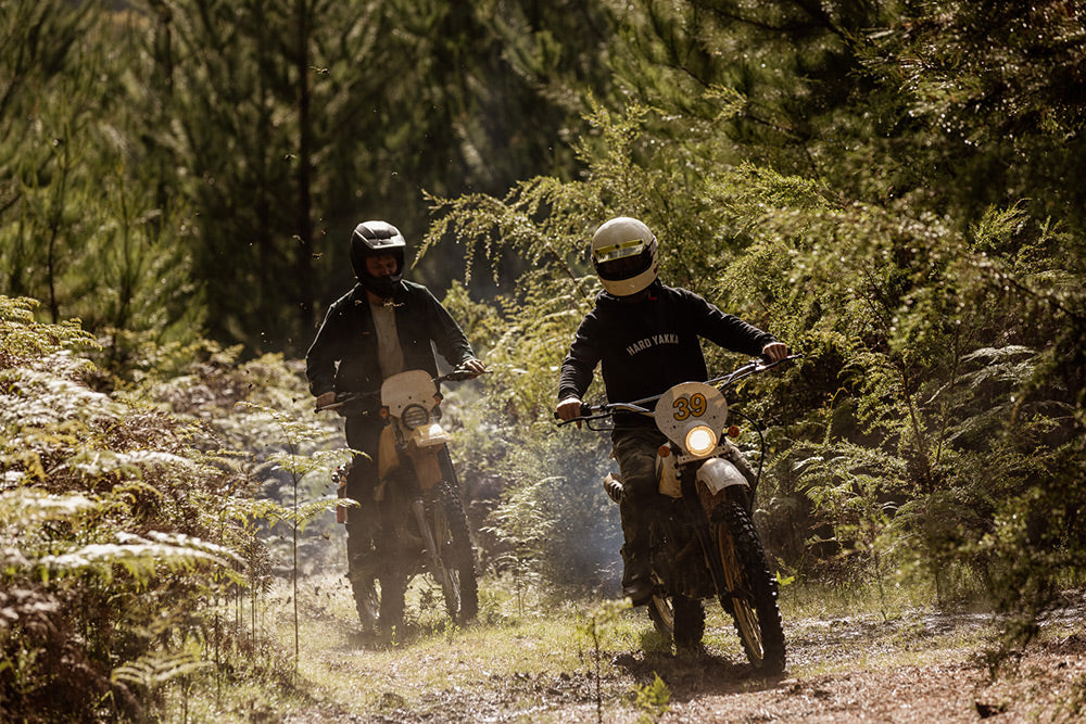 Two people riding dirt bikes on a forest trail