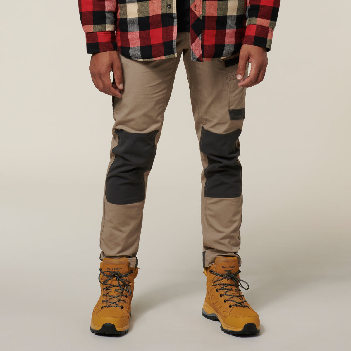 Person wearing a plaid shirt, beige pants with black patches, and yellow boots on a plain background