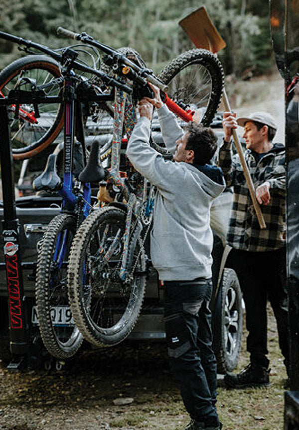 Two people loading bicycles onto a vehicle in a forest setting