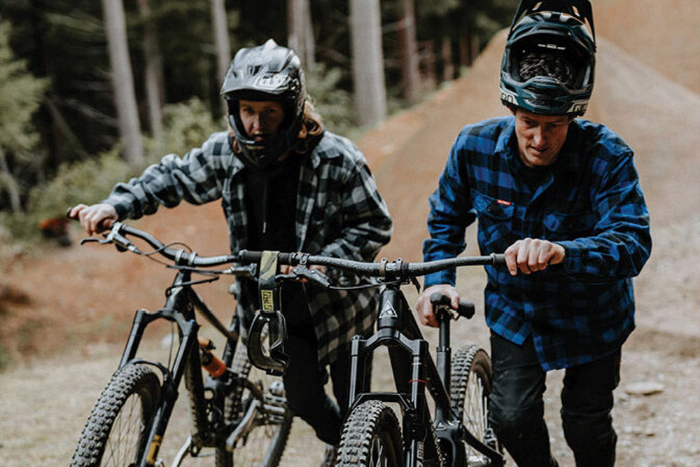 Two individuals with mountain bikes on a trail in a forest setting