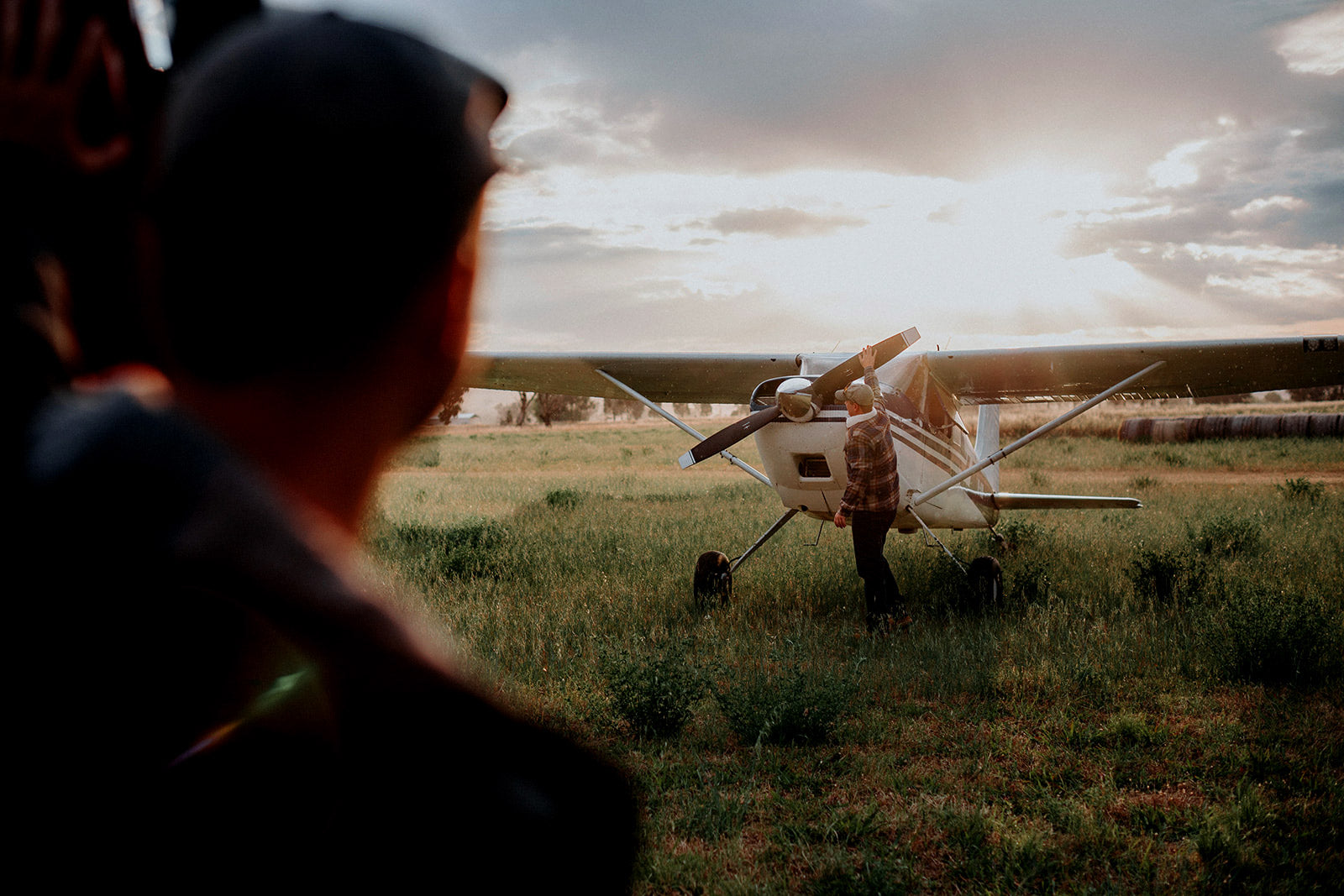 Person standing in a field looking at a small airplane with a cloudy sky.