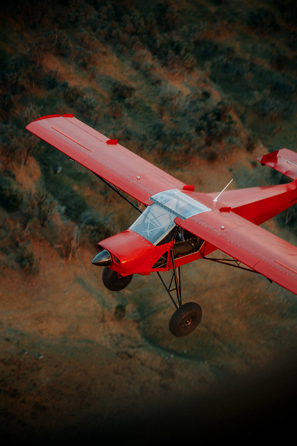 Red airplane flying over a forested area