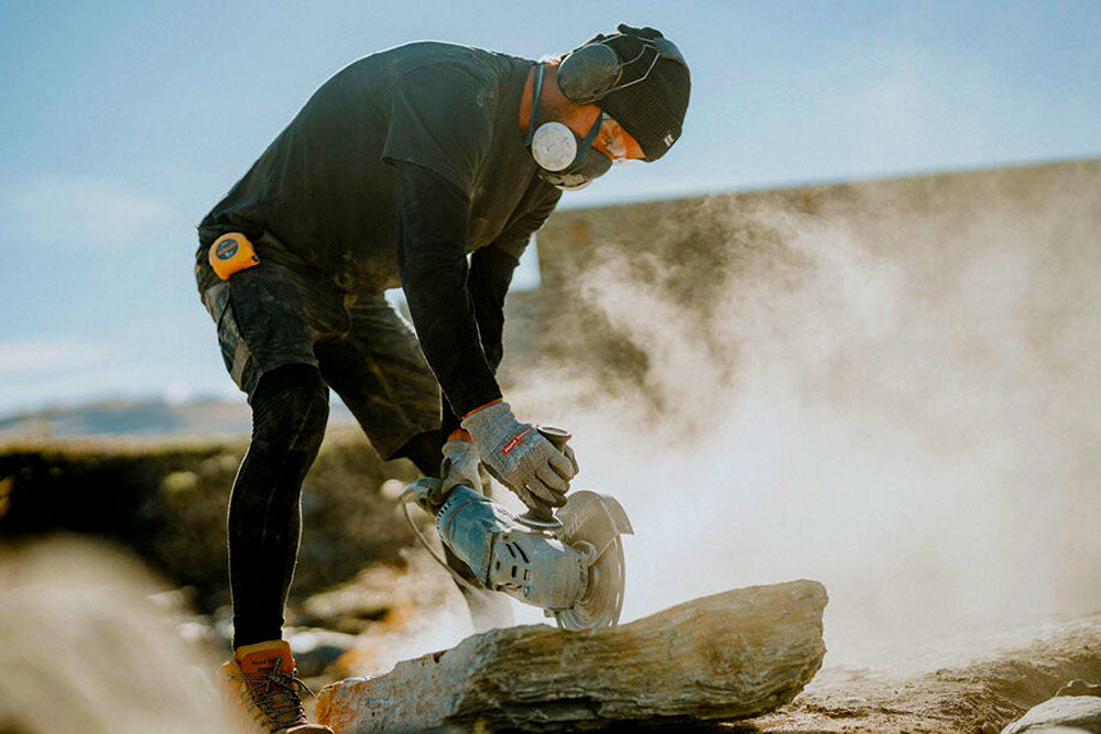 Person using a circular saw to cut a log outdoors with a clear sky.